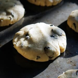 About Snackit Close-up of chocolate chip cookie dough pieces baking on a tray under natural lighting.